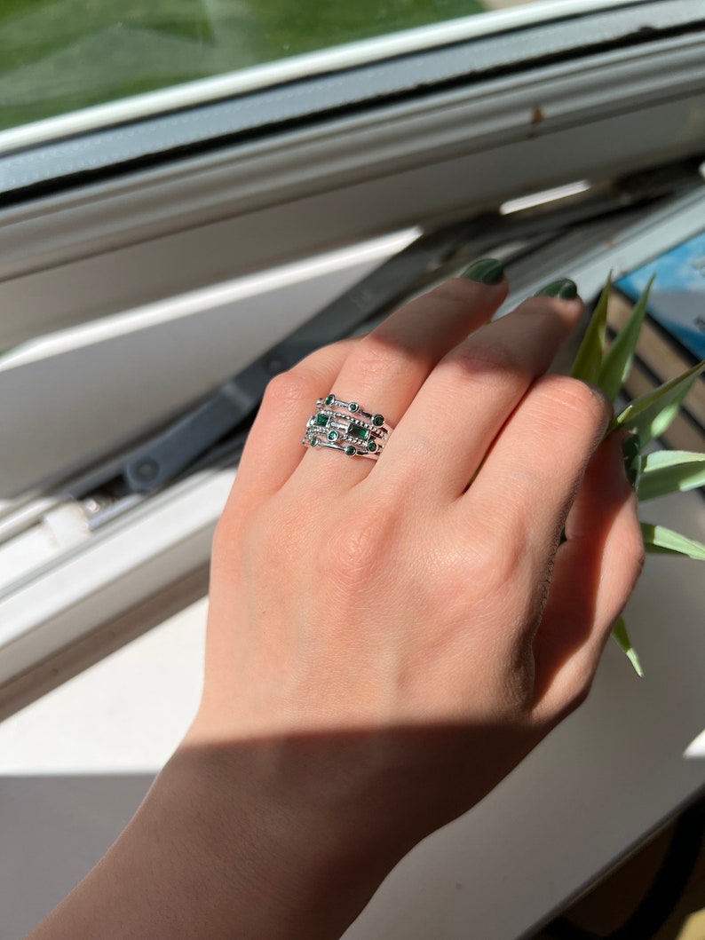 May include: A hand wearing a set of four silver rings with green gemstones. The rings are stacked on each other and have a delicate design.