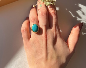 May include: A gold ring with a turquoise oval gemstone. The ring is on a person's finger.