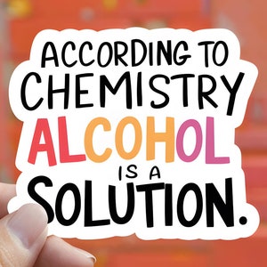 May include: A white sticker with the text "ACCORDING TO CHEMISTRY ALCOHOL IS A SOLUTION." The word "ALCOHOL" is in pink and orange. The sticker is held by a hand against a blurred red background.