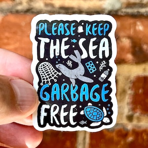 Puede incluir: Una pegatina con un diseño azul y blanco que dice "Por favor, mantén el mar libre de basura". La pegatina presenta una foca de dibujos animados, una tortuga y una red.