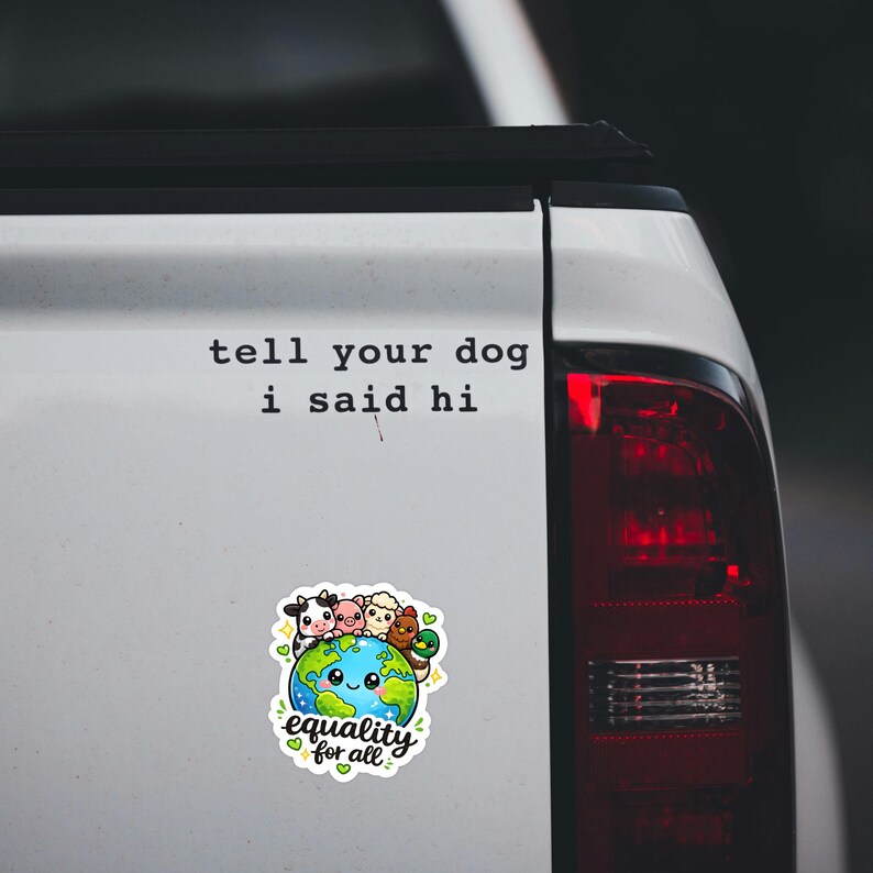 May include: A white vinyl sticker featuring the black text 'tell your dog i said hi' above a colorful illustration of a smiling Earth globe surrounded by a cow, pig, sheep, chicken, and duck, with the text 'equality for all' at the bottom.
