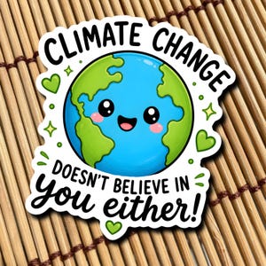 以下が含まれることがあります： 「CLIMATE CHANGE」と「DOESN'T BELIEVE IN you either!」という黒い文字が入った白いステッカー。緑の大陸、青い海、ピンクの頬をした笑顔の地球が描かれ、緑のハートと星で囲まれています。