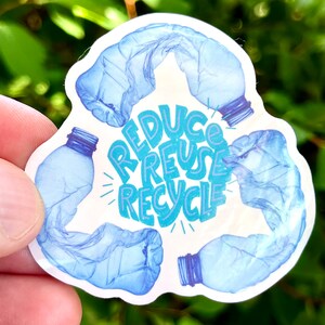Puede incluir: Una pegatina blanca con un símbolo de reciclaje azul hecho de botellas de agua de plástico arrugadas. Las palabras "Reduce Reutiliza Recicla" están escritas en azul y morado dentro del símbolo.