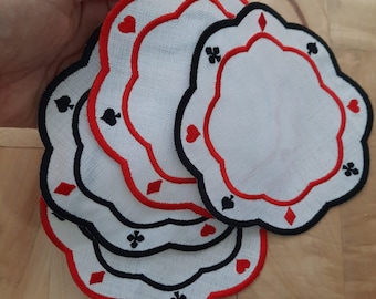 Peut inclure: Ensemble de quatre dessous-de-verre en tissu blanc avec des symboles de cartes à jouer brodés en rouge et noir. Les dessous-de-verre sont superposés.