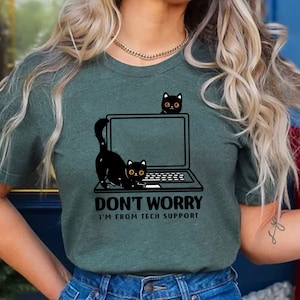 May include: A green t-shirt with a black cat peeking out from behind a laptop. The text on the shirt reads "Don't Worry I'm From Tech Support."