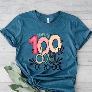 May include: Teal blue t-shirt with a colorful graphic that says "Happy 100th day of school".