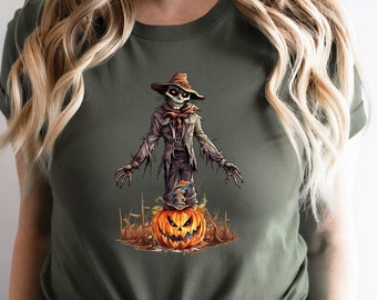 May include: A green t-shirt with a graphic of a spooky scarecrow standing on a jack-o'-lantern. The scarecrow is wearing a brown hat and has a skeletal face.