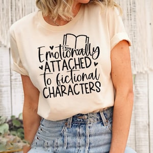 May include: A beige t-shirt with black text that reads "Emotionally Attached to Fictional Characters" and a small graphic of two books.