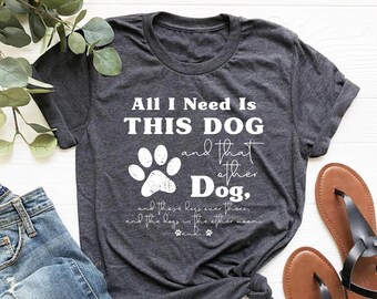May include: A dark gray t-shirt with the text "All I Need Is THIS DOG and that other Dog," and a white paw print graphic.