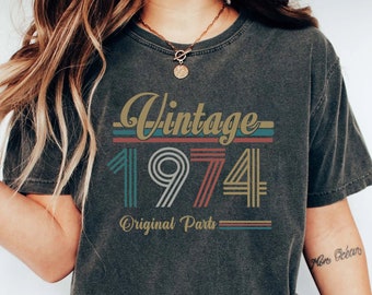 以下が含まれることがあります： 「Vintage 1974 Original Parts」と書いてあるヴィンテージスタイルのグラフィックがプリントされたダークグレーのTシャツ。グラフィックは虹色で、白いアウトラインがあります。