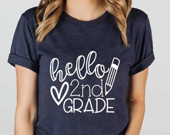 Könnte beinhalten: Ein marineblaues T-Shirt mit weißem Text, der "hello 2nd grade" mit einem Herz und einem Bleistift sagt.