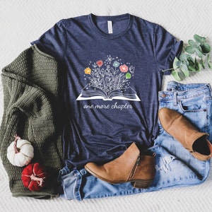 May include: A navy blue t-shirt with a white graphic of an open book with flowers growing out of it. The text "one more chapter" is printed below the book.