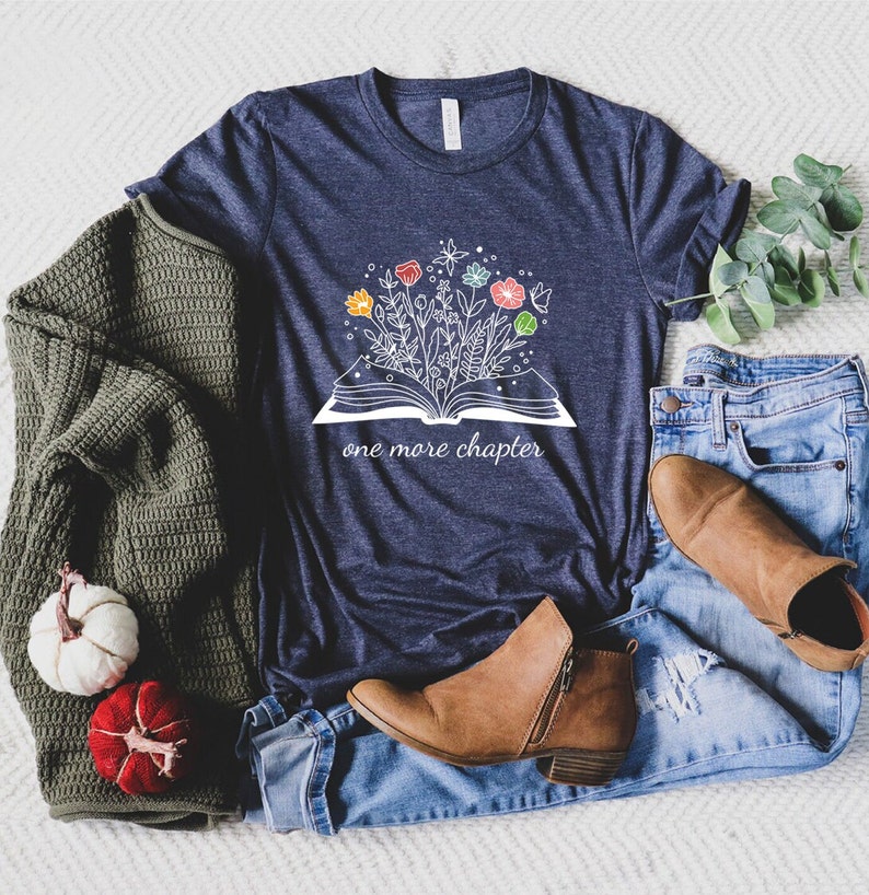 May include: A navy blue t-shirt with a white graphic of an open book with flowers growing out of it. The text "one more chapter" is printed below the book.