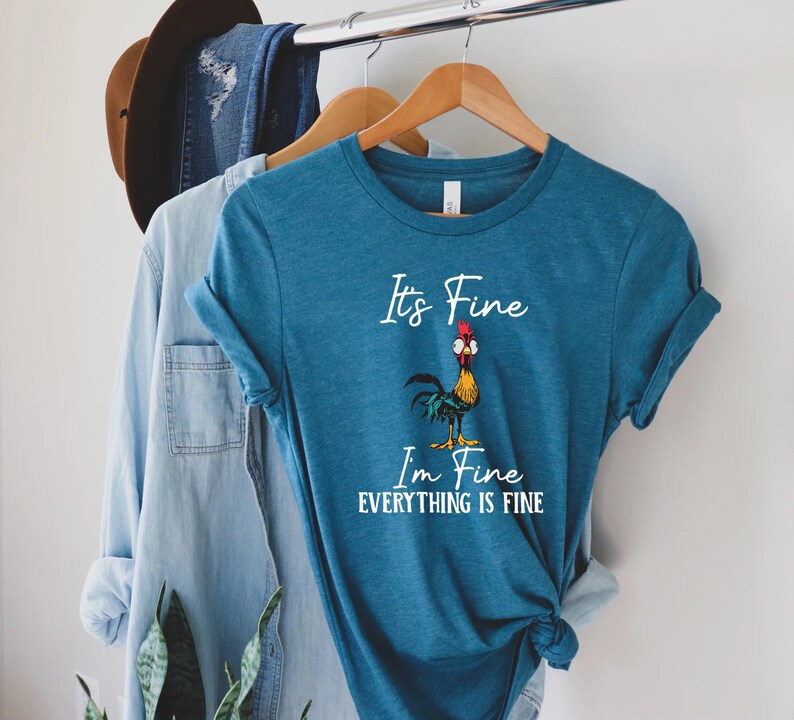 May include: A teal blue t-shirt with a white rooster graphic and the text "It's Fine I'm Fine Everything Is Fine".