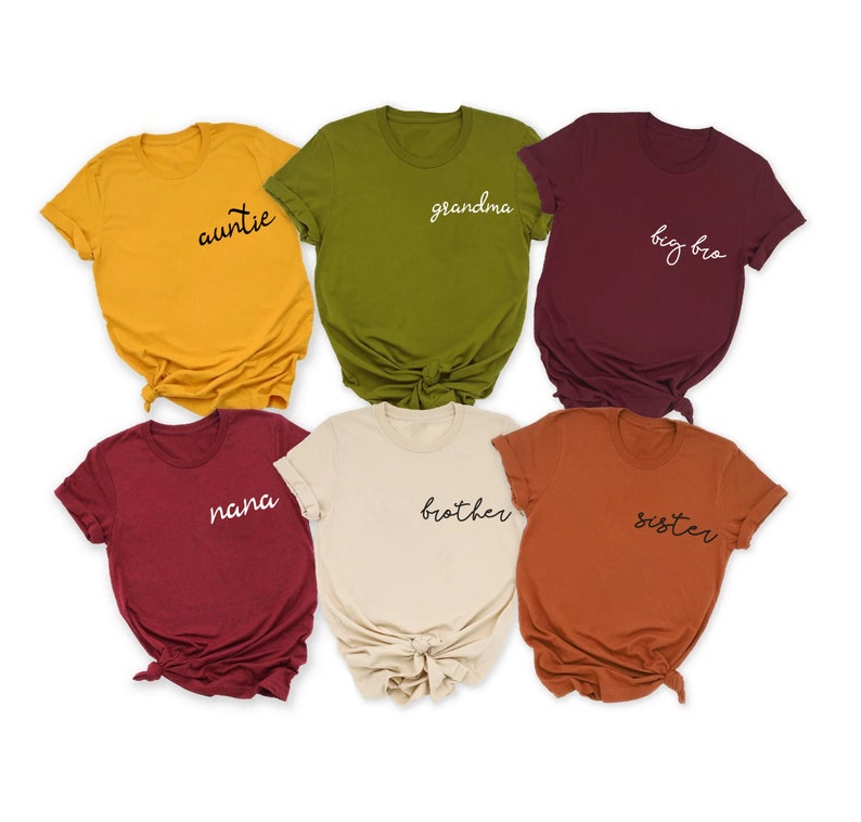 Peut inclure: Six t-shirts de diff&eacute;rentes couleurs avec des titres de membres de la famille imprim&eacute;s dessus en &eacute;criture noire et blanche. Les t-shirts sont : jaune avec "auntie", vert avec "grandma", bordeaux avec "big bro", bordeaux avec "nana", beige avec "brother", et orange avec "sister".