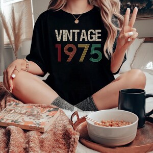 May include: A black t-shirt with the text "Vintage 1975" in rainbow colors. The text is in a retro font style.