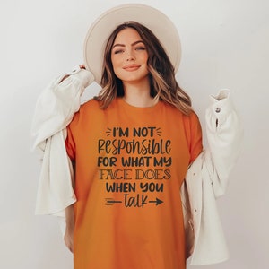 K&ouml;nnte beinhalten: Orangefarbenes T-Shirt mit schwarzem Text, der "Ich bin nicht verantwortlich f&uuml;r das, was mein Gesicht tut, wenn du sprichst" lautet, mit Pfeilen auf beiden Seiten des Textes.