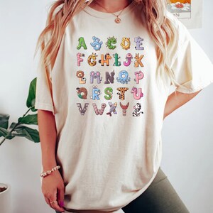 May include: A white t-shirt with a colorful alphabet printed on the front. Each letter is paired with a cartoon animal.