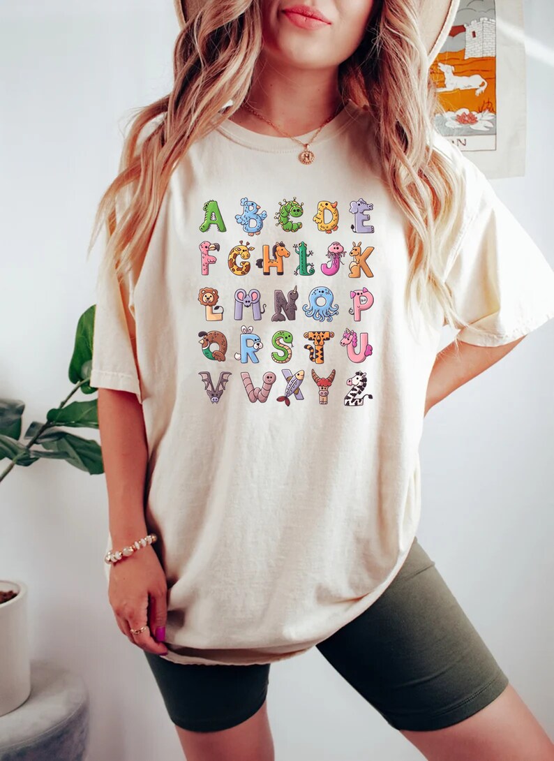 May include: A white t-shirt with a colorful alphabet printed on the front. Each letter is paired with a cartoon animal.