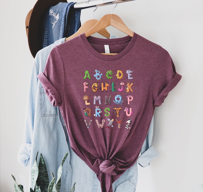 May include: A maroon t-shirt with a colorful alphabet printed on the front. Each letter is decorated with a different animal illustration.