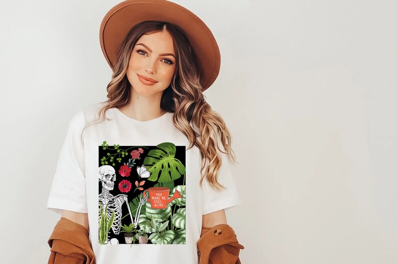 May include: White t-shirt with a black square graphic featuring a skeleton holding a watering can with the text "You make me feel alive". The graphic also includes green and red flowers, butterflies, and various plants.