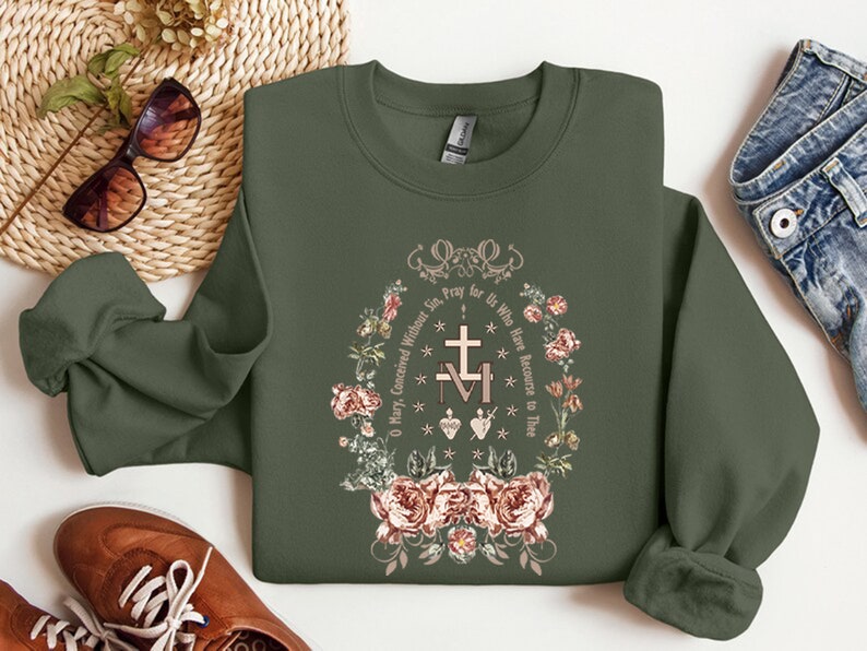 May include: A green sweatshirt with a floral design and the text "O Mary, Conceived Without Sin, Pray for Us Who Have Recourse to Thee."