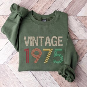 May include: A green sweatshirt with the text "Vintage 1975" in a retro font with colorful stripes.