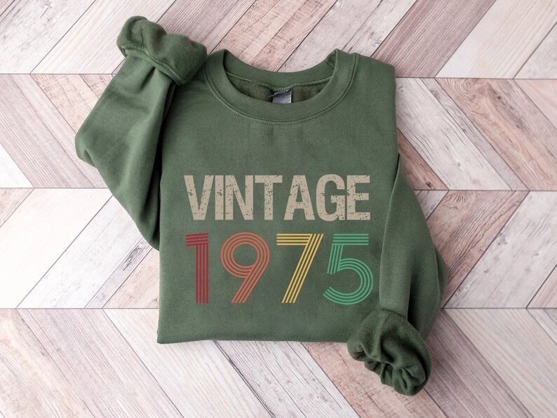May include: A green sweatshirt with the text "Vintage 1975" in a retro font with colorful stripes.