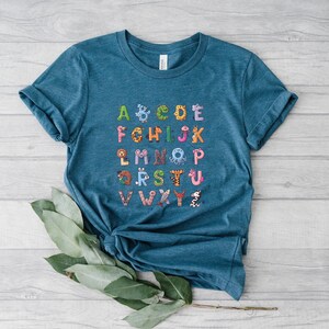 May include: A teal blue t-shirt with a colorful alphabet printed on the front. Each letter is decorated with a different animal illustration.