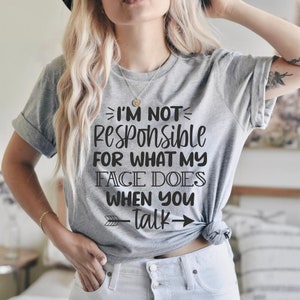 K&ouml;nnte beinhalten: Graues T-Shirt mit dem Text "Ich bin nicht verantwortlich f&uuml;r das, was mein Gesicht tut, wenn du sprichst" darauf gedruckt. Der Text ist schwarz und hat einen Pfeil, der nach rechts zeigt.