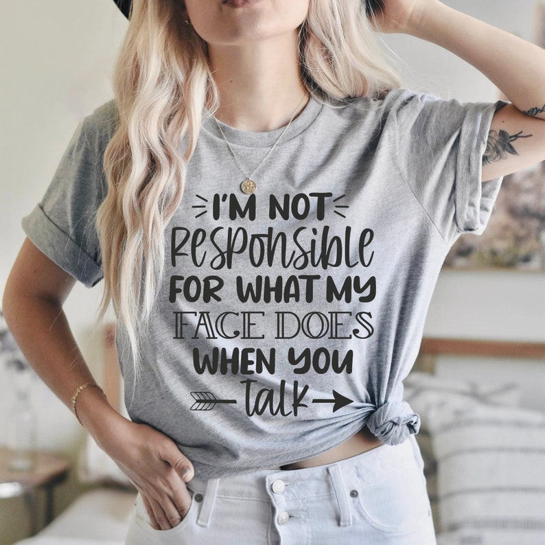 K&ouml;nnte beinhalten: Graues T-Shirt mit dem Text "Ich bin nicht verantwortlich f&uuml;r das, was mein Gesicht tut, wenn du sprichst" darauf gedruckt. Der Text ist schwarz und hat einen Pfeil, der nach rechts zeigt.