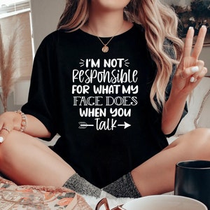 K&ouml;nnte beinhalten: Ein schwarzes T-Shirt mit wei&szlig;em Text, der "Ich bin nicht verantwortlich f&uuml;r das, was mein Gesicht macht, wenn du sprichst" lautet, mit einem wei&szlig;en Pfeil, der nach rechts zeigt, und einem wei&szlig;en Pfeil, der nach links zeigt.