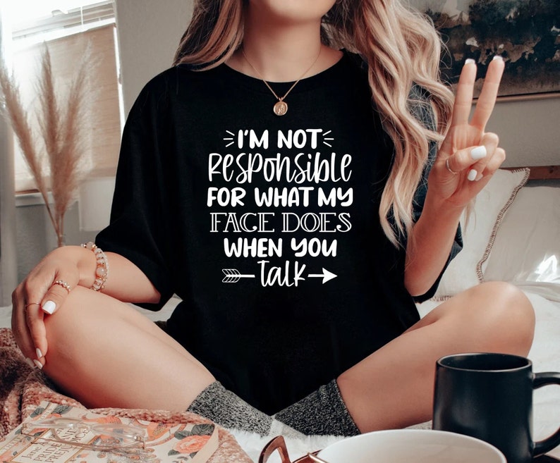 K&ouml;nnte beinhalten: Ein schwarzes T-Shirt mit wei&szlig;em Text, der "Ich bin nicht verantwortlich f&uuml;r das, was mein Gesicht macht, wenn du sprichst" lautet, mit einem wei&szlig;en Pfeil, der nach rechts zeigt, und einem wei&szlig;en Pfeil, der nach links zeigt.