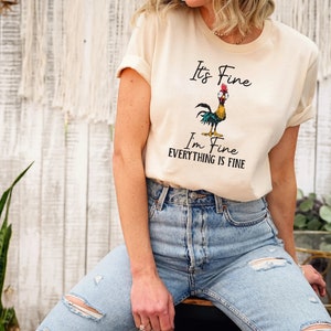 May include: A beige t-shirt with a cartoon rooster and the text "It's Fine I'm Fine Everything is Fine".