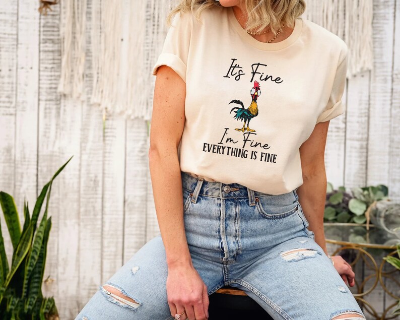 May include: A beige t-shirt with a cartoon rooster and the text "It's Fine I'm Fine Everything is Fine".