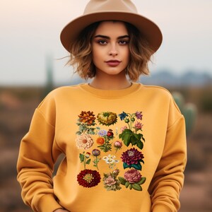 May include: A yellow sweatshirt with a floral print featuring a variety of flowers and leaves in shades of red, pink, yellow, and green.