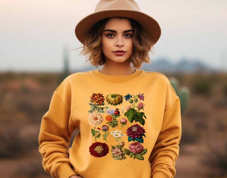 May include: A yellow sweatshirt with a floral print featuring a variety of flowers and leaves in shades of red, pink, yellow, and green.