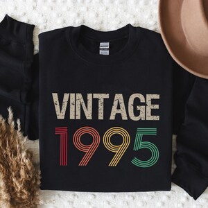 May include: Black sweatshirt with a vintage 1995 design in rainbow colors. The text "Vintage" is in a distressed font.
