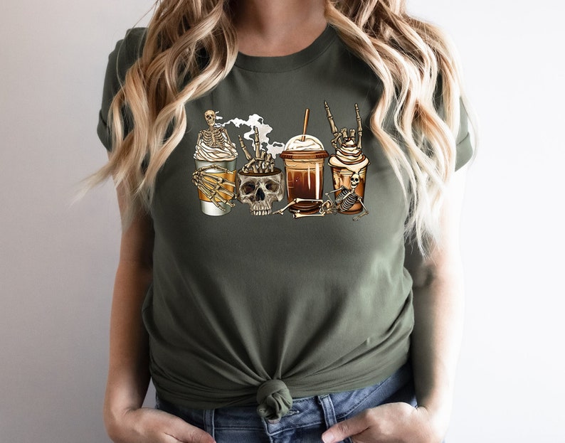 K&ouml;nnte beinhalten: Ein gr&uuml;nes T-Shirt mit einem Motiv von Kaffeetassen und Sch&auml;deln, wobei Skelette die Tassen halten. Die Kaffeetassen haben Schlagsahne und einen Strohhalm.