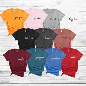 Peut inclure: Assortiment de t-shirts de diff&eacute;rentes couleurs avec des titres de membres de la famille imprim&eacute;s en blanc sur le devant. Les titres incluent : "papa", "grand-m&egrave;re", "fr&egrave;re", "grand fr&egrave;re", "s&oelig;ur", "p&egrave;re", "m&egrave;re", "tante", "mamie".