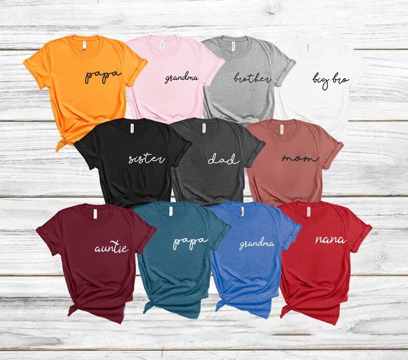 Peut inclure: Assortiment de t-shirts de diff&eacute;rentes couleurs avec des titres de membres de la famille imprim&eacute;s en blanc sur le devant. Les titres incluent : "papa", "grand-m&egrave;re", "fr&egrave;re", "grand fr&egrave;re", "s&oelig;ur", "p&egrave;re", "m&egrave;re", "tante", "mamie".