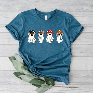 May include: A teal blue t-shirt featuring a graphic of four white ghosts wearing mushroom hats. The mushrooms are red, brown, and green.