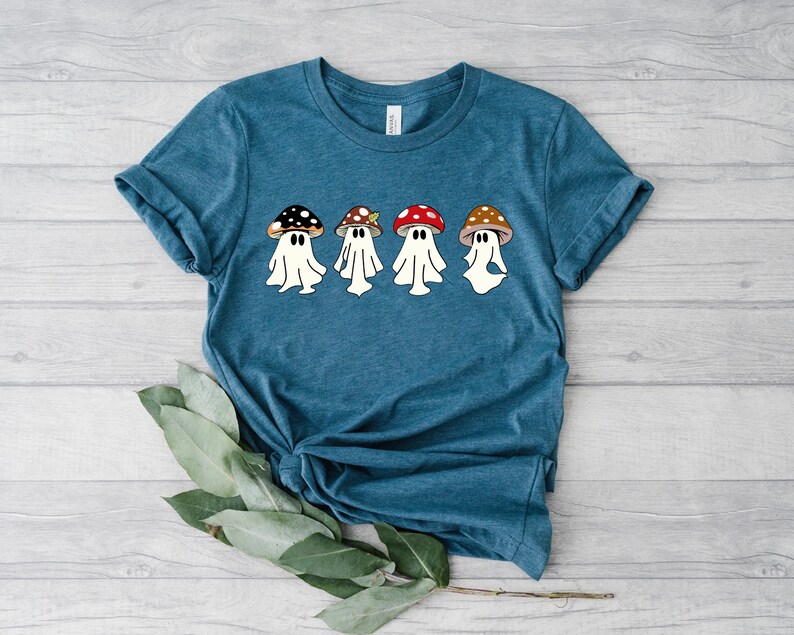 May include: A teal blue t-shirt featuring a graphic of four white ghosts wearing mushroom hats. The mushrooms are red, brown, and green.