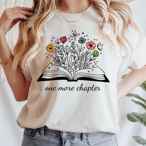 May include: White t-shirt with a black and white illustration of an open book with flowers growing out of it. The text "one more chapter" is printed below the book.