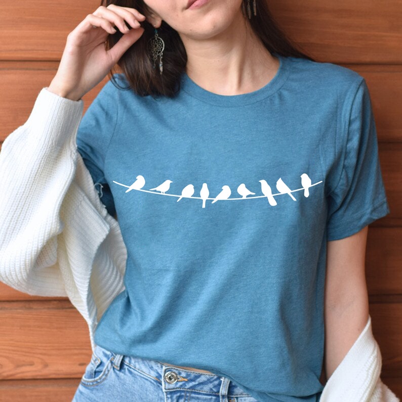 May include: A teal blue t-shirt with a white graphic of a line of birds perched on a wire.