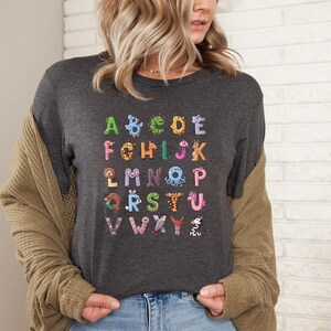 May include: A dark gray t-shirt with a colorful alphabet printed on the front. Each letter is formed by a different animal.