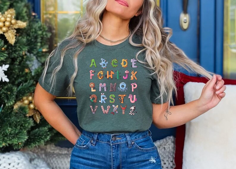 May include: A green t-shirt with a colorful alphabet printed on the front. Each letter is decorated with a different animal illustration.