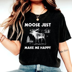 May include: Black t-shirt with a white graphic of a moose and the text "MOOSE JUST MAKE ME HAPPY". The moose illustration includes trees and mountains. The shirt is a casual style.