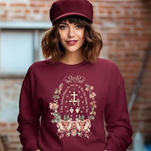 May include: A maroon sweatshirt with a floral design and the text "O Mary, Conceived Without Sin, Pray for Us Who Have Recourse to Thee" in a circle around a cross.