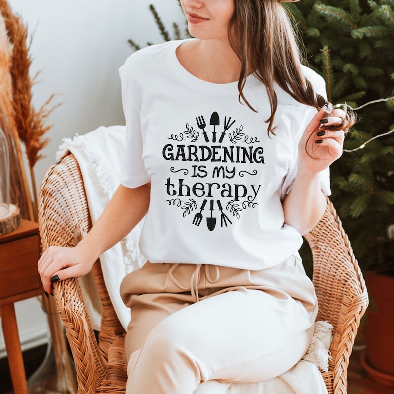 May include: White t-shirt with black text that reads "Gardening is my therapy" with a design of gardening tools and leaves around the text.